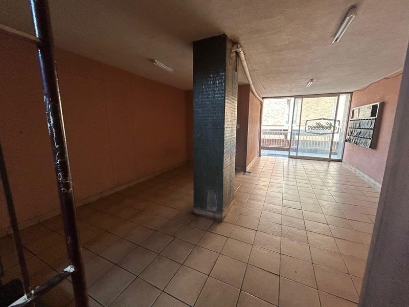 An empty apartment building entrance lobby featuring tiled flooring, a central structural column, and wall-mounted mailboxes leading to a sliding glass door.
