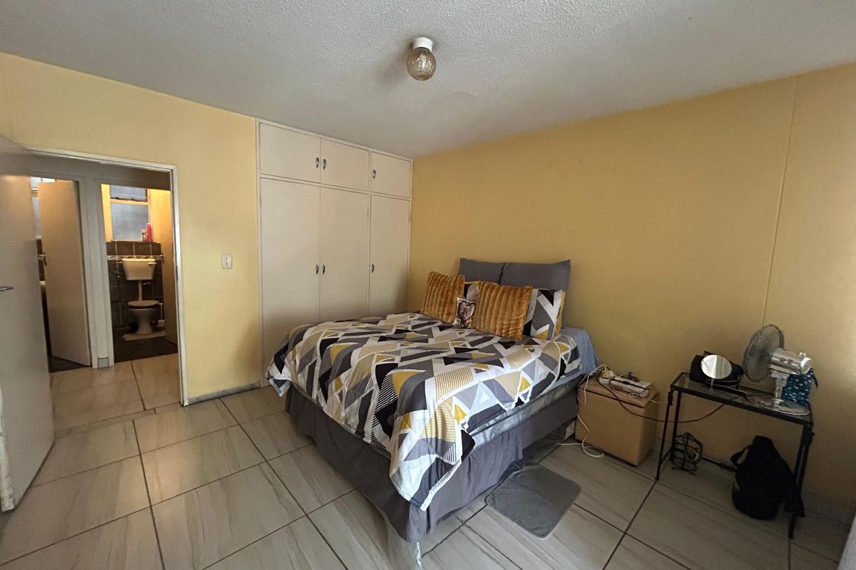 A bedroom featuring tiled flooring and built-in cupboards, with an adjoining bathroom visible through the doorway.