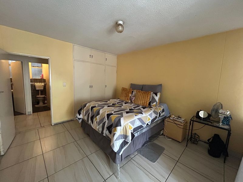 A bedroom featuring tiled flooring and built-in cupboards, with an adjoining bathroom visible through the doorway.