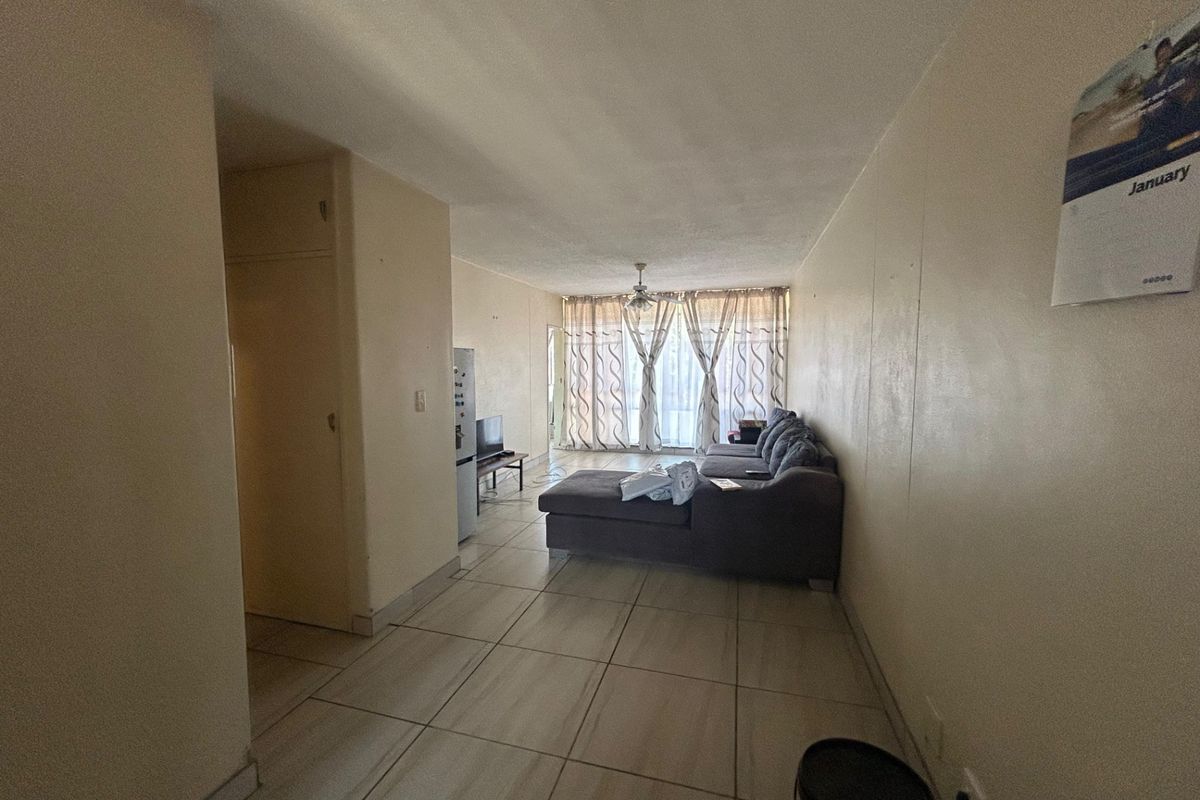 A living room area featuring tiled flooring, a ceiling fan, and a built-in cupboard, with access to a balcony through sliding glass doors.