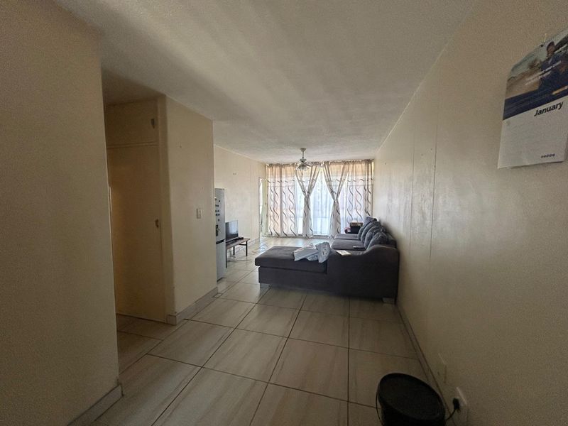 A living room area featuring tiled flooring, a ceiling fan, and a built-in cupboard, with access to a balcony through sliding glass doors.