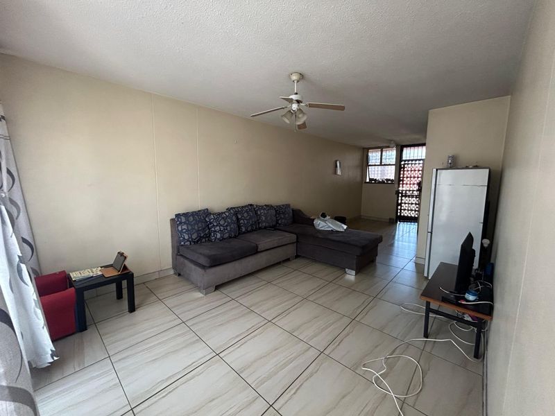 Open plan living area featuring tiled flooring and a ceiling fan, providing a functional space with direct access to the exterior security gate.