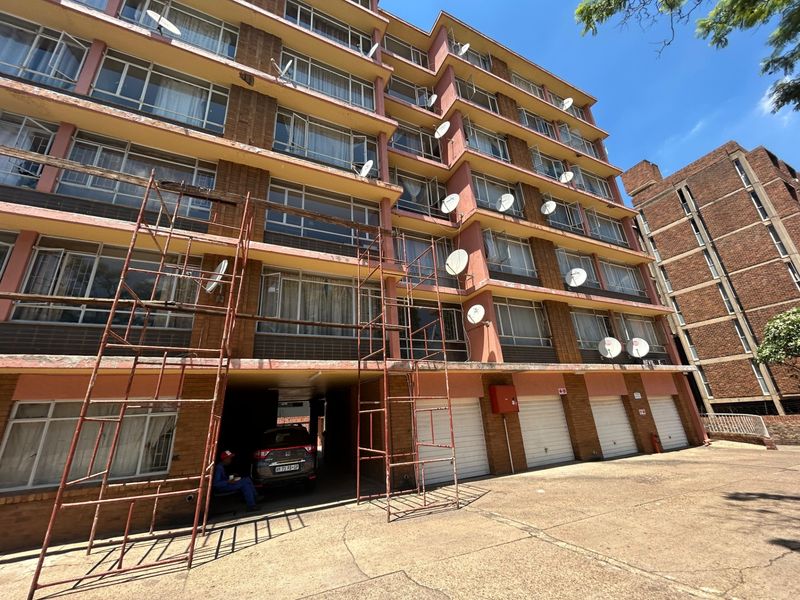 Front elevation of a multi-story apartment building featuring brick facade, multiple satellite dishes, and ground-level garage access with active maintenance scaffolding.