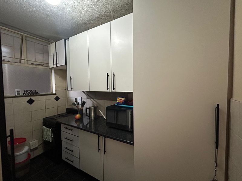Compact kitchen featuring white built-in cabinetry, dark countertops, and tiled backsplash, providing a functional workspace with essential storage and cooking facilities.