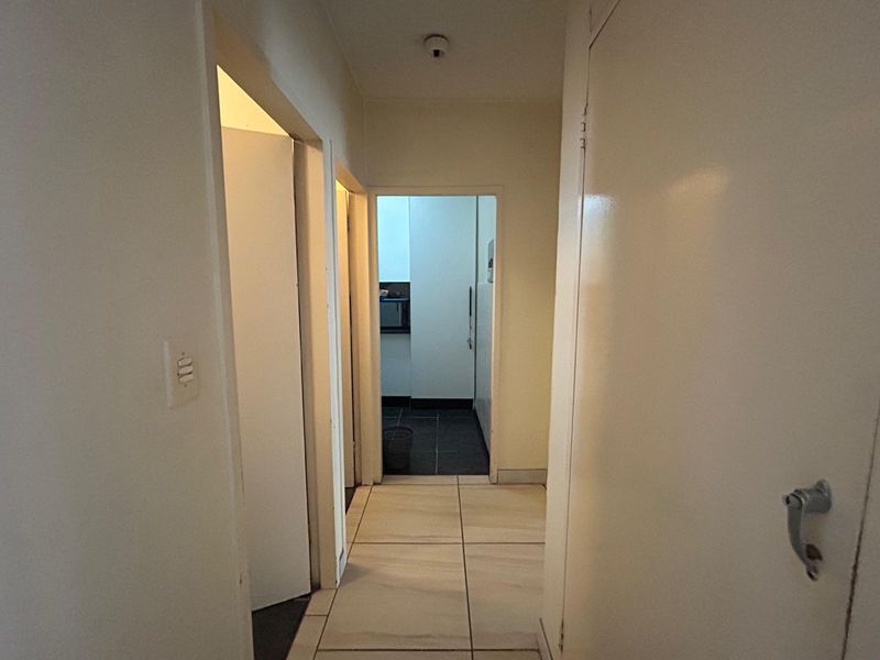 A functional apartment hallway with tiled flooring, providing access to multiple rooms including a view into the kitchen area.