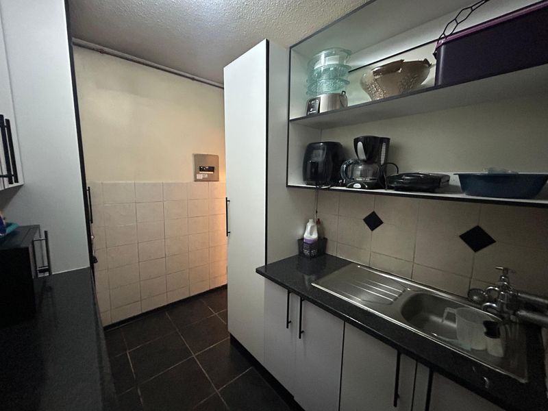 A compact kitchen area featuring built-in cabinetry, a stainless steel sink, tiled backsplash, and dark tiled flooring.