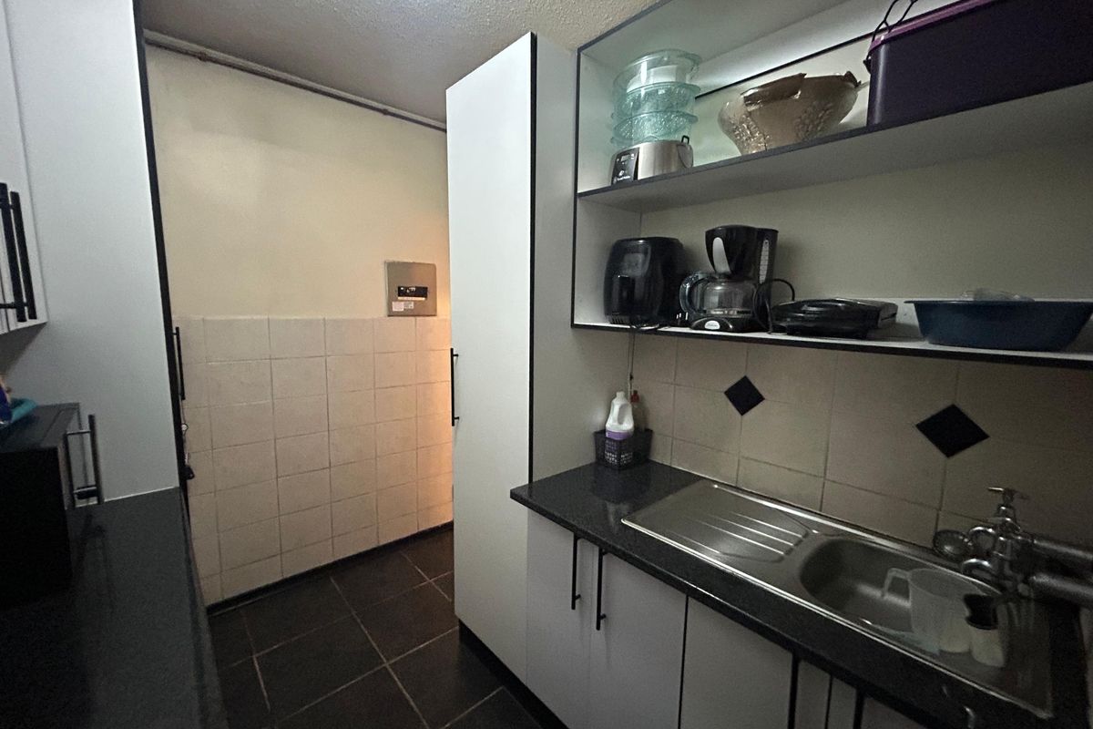 A compact kitchen area featuring built-in cabinetry, a stainless steel sink, tiled backsplash, and dark tiled flooring.