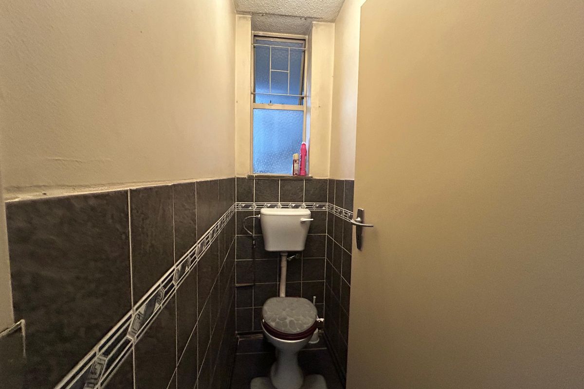 A compact, tiled guest toilet featuring a standard ceramic toilet suite and a small window with security bars.