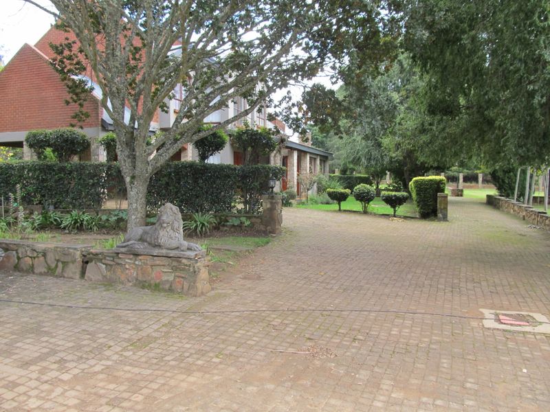 A view of the front exterior featuring a paved driveway, mature trees, landscaped hedges, and a brick residential building facade.
