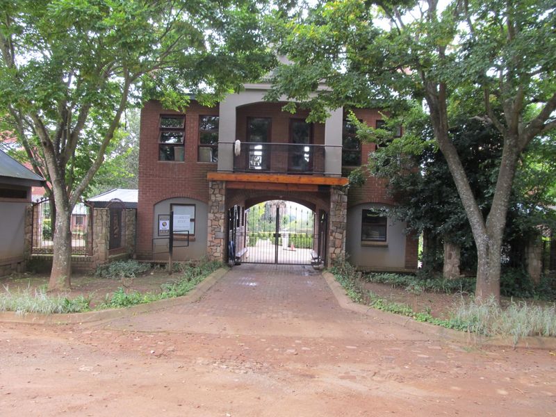 Front elevation of a brick and stone residential building featuring a gated entrance, paved driveway, and a second-story balcony.