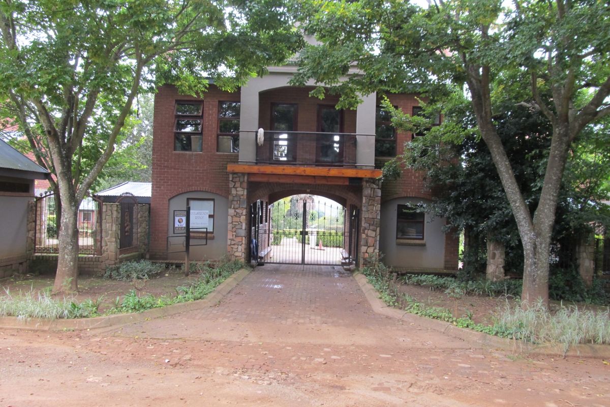 Front elevation of a brick and stone residential building featuring a gated entrance, paved driveway, and a second-story balcony.