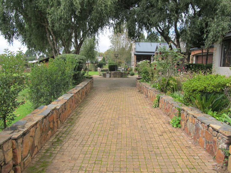 A landscaped garden path featuring stone retaining walls and mature trees leading towards the property entrance.