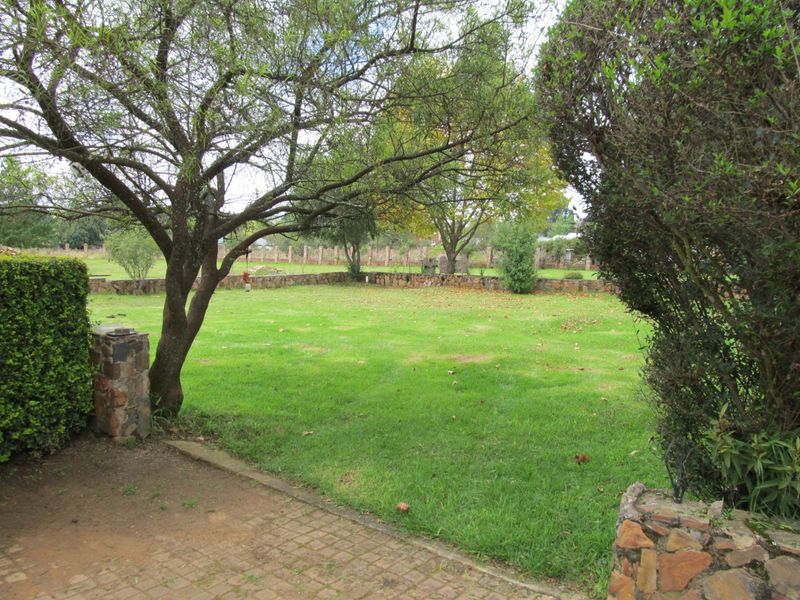 A spacious, well-maintained garden featuring a lush lawn, mature trees, and a stone retaining wall, providing a peaceful outdoor setting.