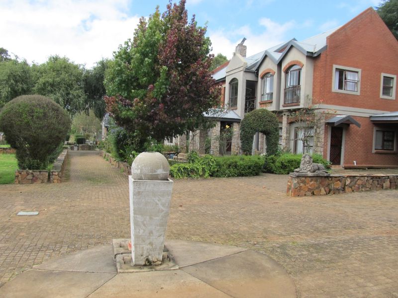 Front view of a multi-story brick residential property featuring a paved driveway, stone retaining walls, and established garden landscaping.