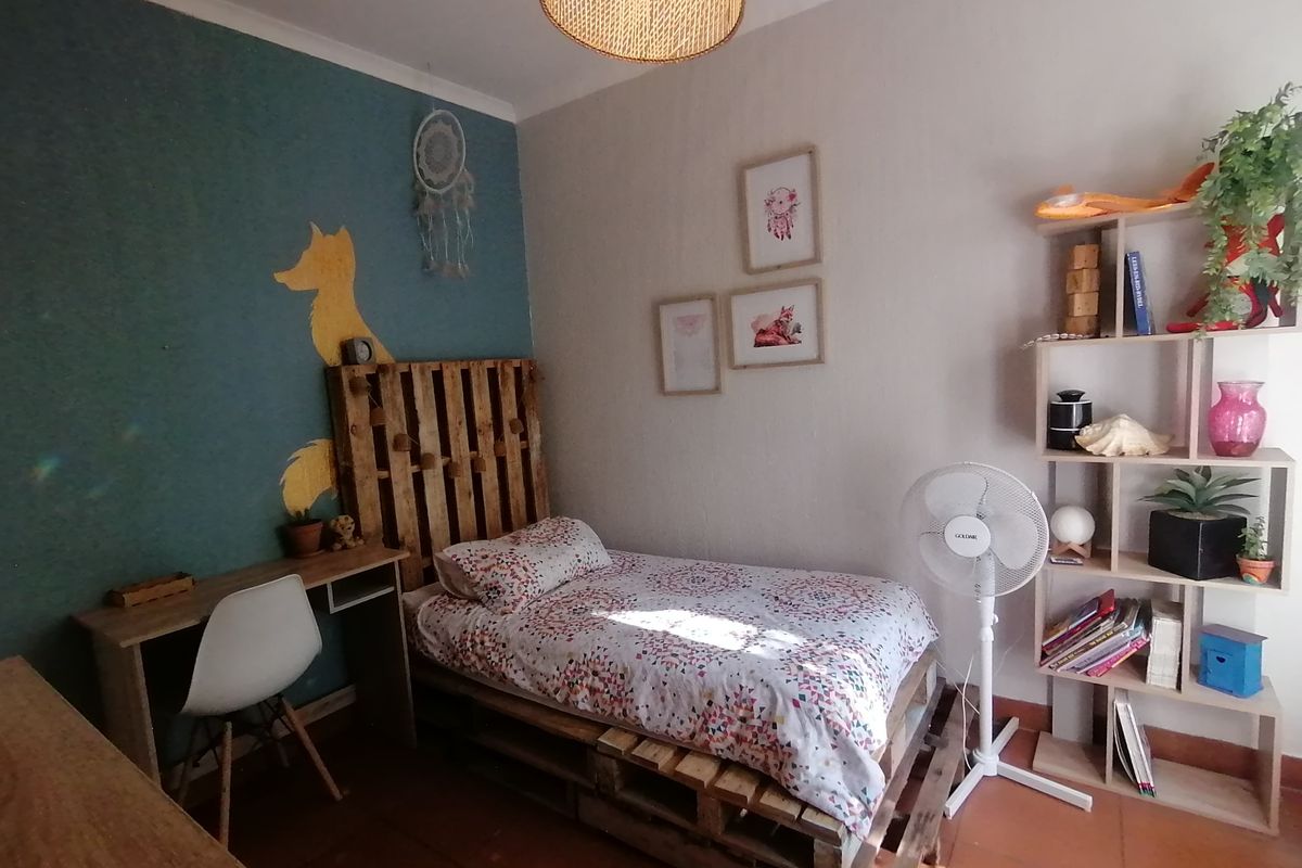 A cozy bedroom featuring tiled flooring and a decorative accent wall, providing a functional space for rest and study.
