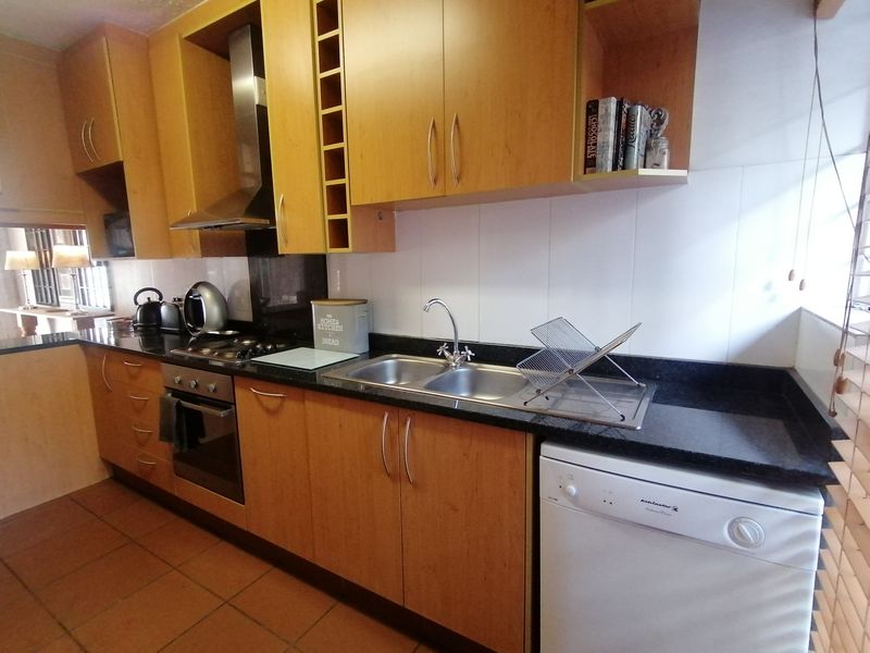 A functional kitchen featuring laminate cabinetry, granite countertops, a stainless steel double sink, built-in oven, gas hob, and tiled flooring.