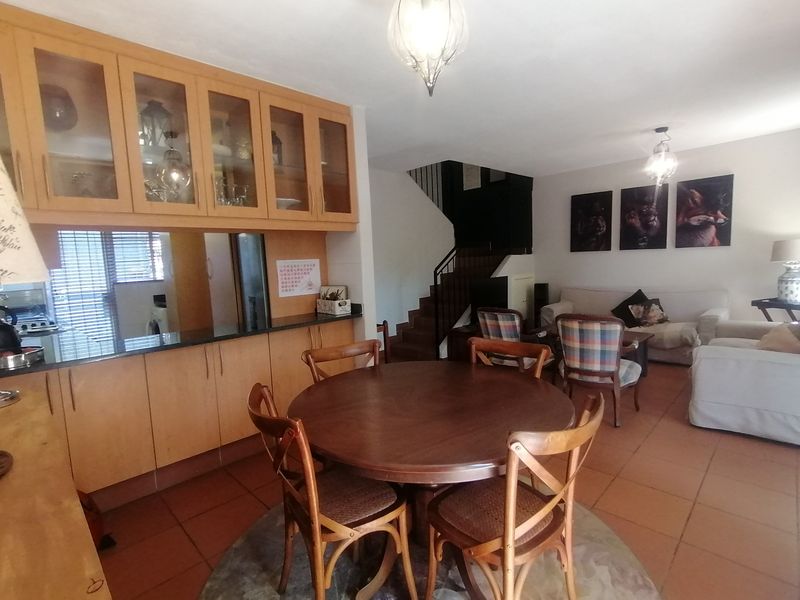 Open-plan living and dining area featuring tiled floors, built-in kitchen cabinetry with glass display units, and a staircase leading to the upper level.