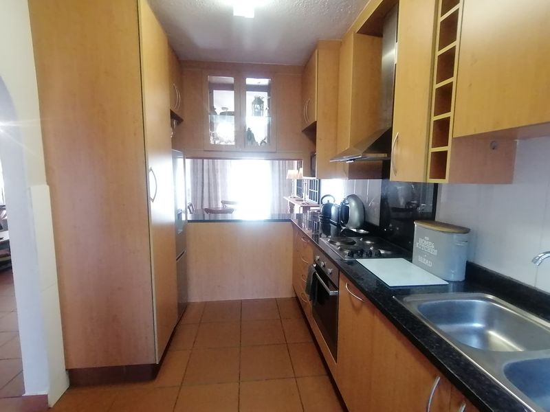 A functional galley-style kitchen featuring wood-finish cabinetry, granite countertops, integrated appliances, and tiled flooring, offering a practical layout for daily meal preparation.