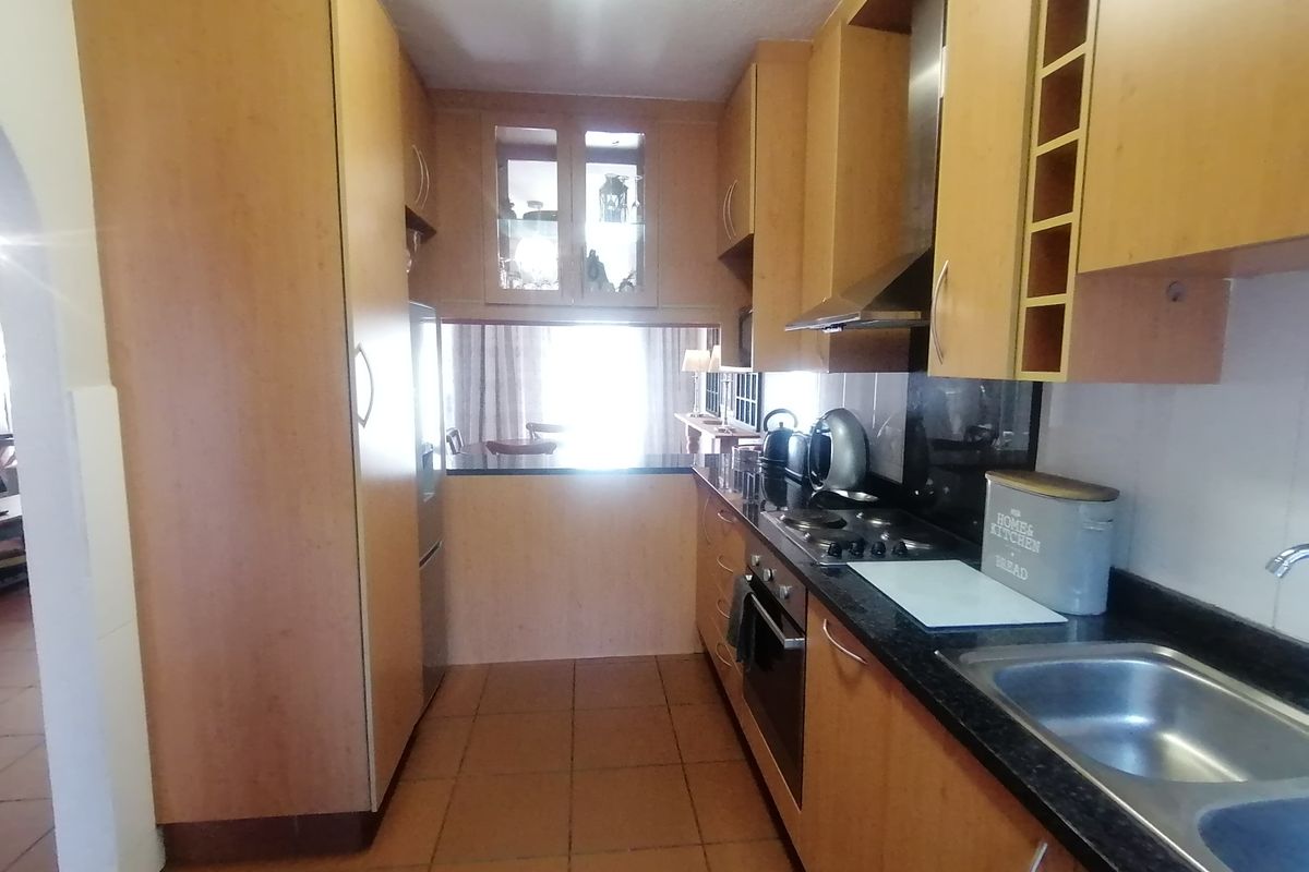 A functional galley-style kitchen featuring wood-finish cabinetry, granite countertops, integrated appliances, and tiled flooring, offering a practical layout for daily meal preparation.