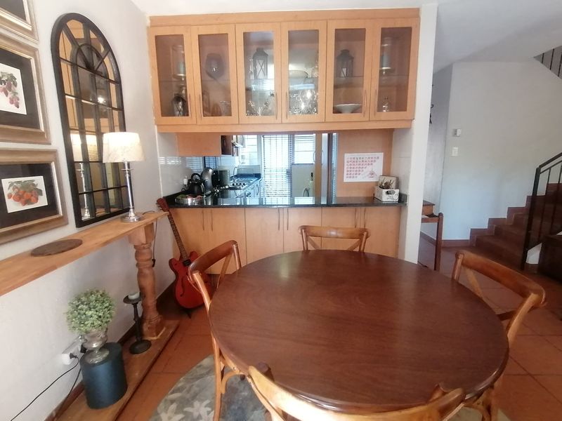 Open plan dining area featuring built-in wooden cabinetry with glass display units, granite countertops, and tiled flooring, adjacent to a staircase.
