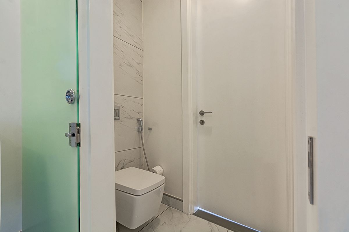 A modern, compact bathroom featuring marble-effect tiling, a wall-mounted toilet with a bidet spray, and a frosted glass door.