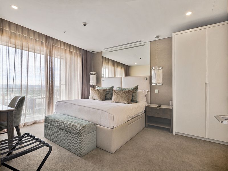 A well-appointed bedroom featuring a built-in wardrobe, mirrored wall accents, recessed lighting, and floor-to-ceiling curtains with access to an outdoor balcony.