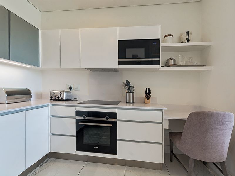 Modern kitchen featuring sleek white cabinetry, integrated appliances including an oven and microwave, stone countertops, and clean, minimalist finishes.