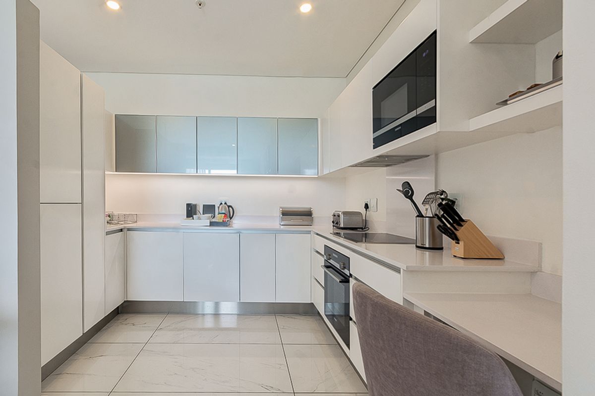 Modern kitchen featuring sleek white cabinetry, stone countertops, integrated appliances, and polished tiled flooring with recessed ceiling lighting.