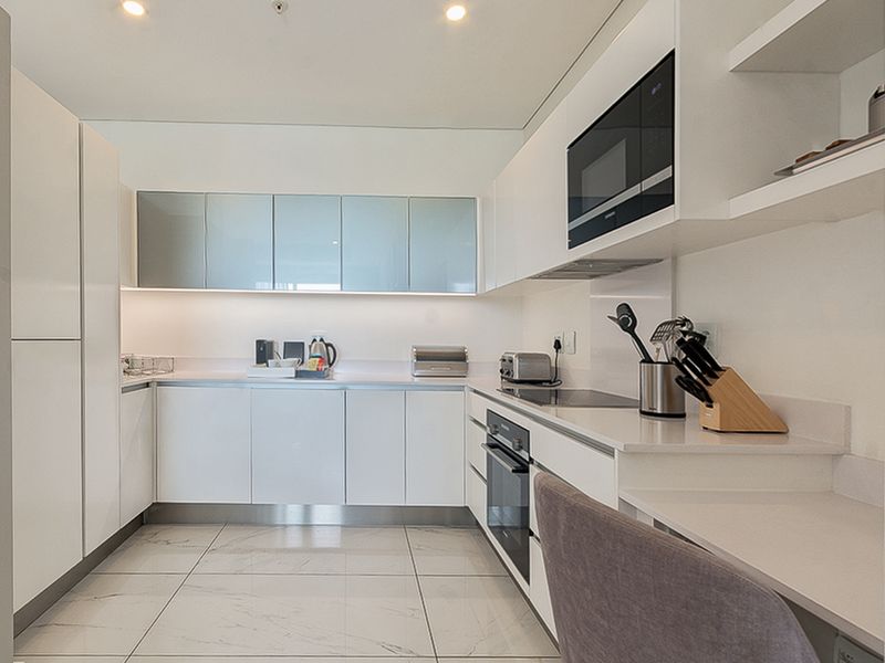 Modern kitchen featuring sleek white cabinetry, stone countertops, integrated appliances, and polished tiled flooring with recessed ceiling lighting.