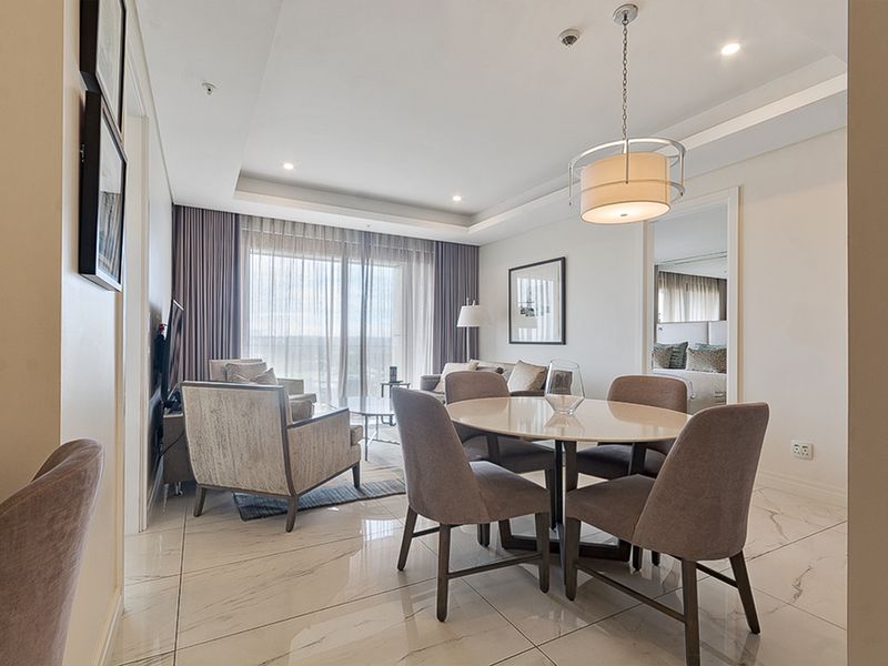A bright open-plan living and dining area featuring polished marble-look floor tiles, recessed ceiling lighting, and large sliding doors leading to a balcony.