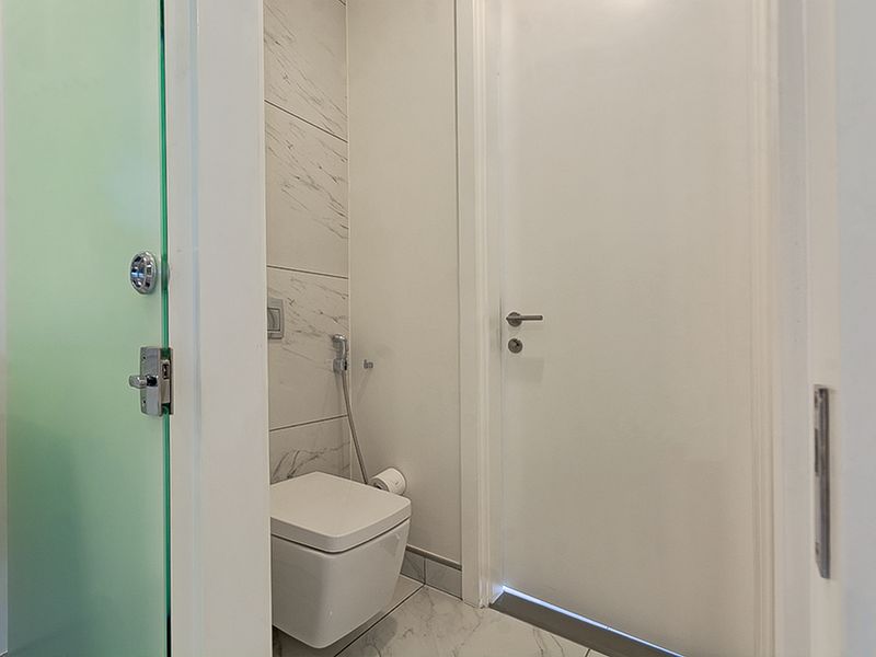 A modern, compact bathroom featuring marble-effect tiling, a wall-mounted toilet with a bidet spray, and a frosted glass door.
