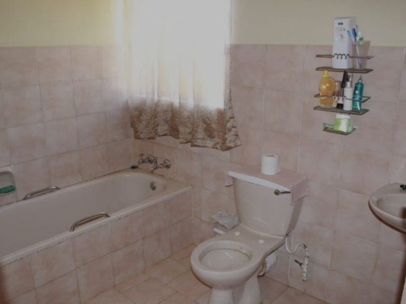 A functional bathroom featuring a bathtub, toilet, and washbasin with neutral wall tiling throughout.