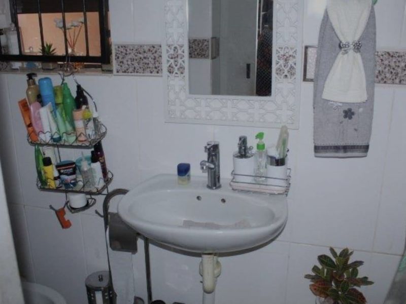 A functional bathroom featuring a pedestal basin with chrome mixer tap and tiled walls with decorative accents.