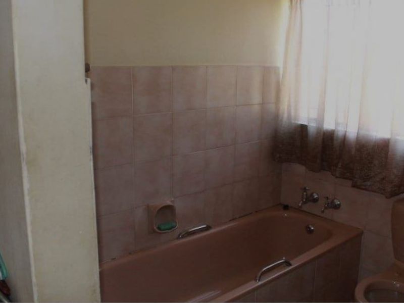 A dated bathroom featuring a built-in bathtub, toilet, and ceramic wall tiling, offering potential for a modern renovation.