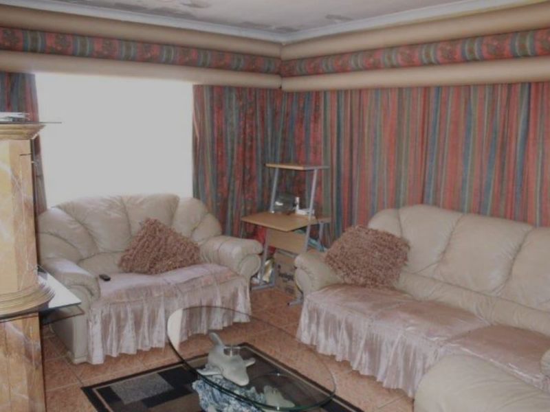 A living room featuring tiled flooring and coved ceilings, currently showing signs of wear and dated decorative elements.