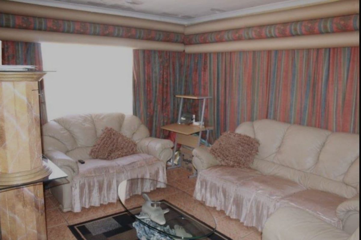 A living room featuring tiled flooring and coved ceilings, currently showing signs of wear and dated decorative elements.