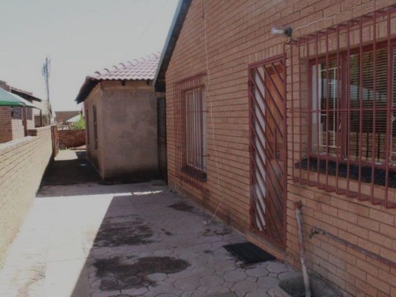 A side view of the property featuring face brick exterior walls, security bars on windows, and a paved walkway along the boundary wall.