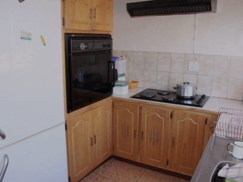A functional kitchen featuring dated wooden cabinetry, a built-in oven, hob, extractor fan, and tiled backsplash with a stainless steel sink.