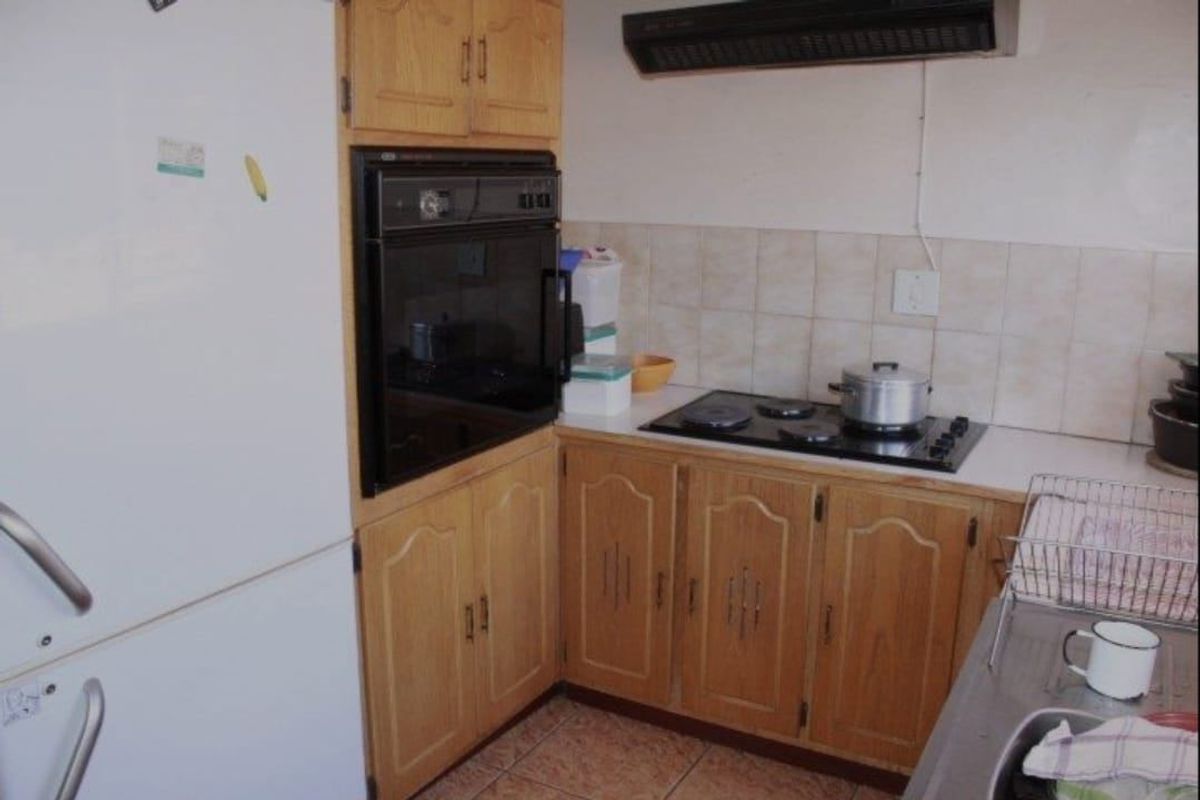 A functional kitchen featuring dated wooden cabinetry, a built-in oven, hob, extractor fan, and tiled backsplash with a stainless steel sink.