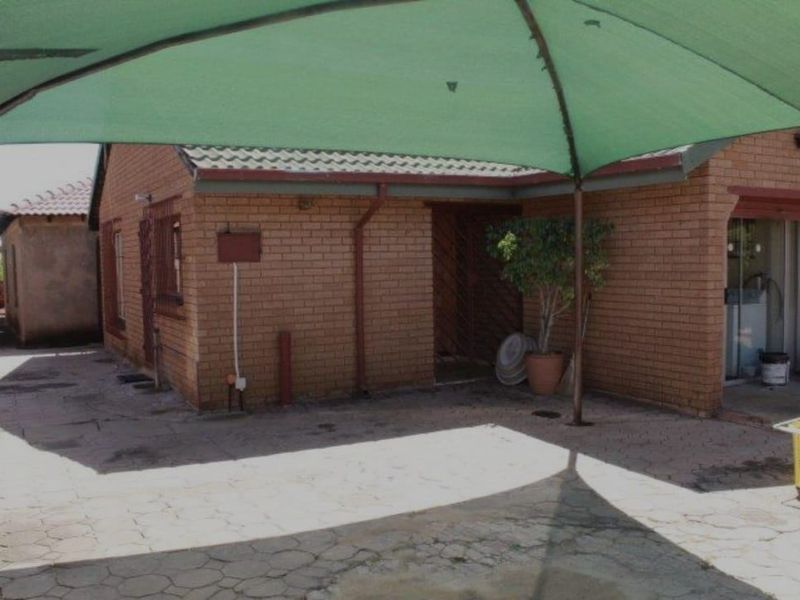 Rear exterior view of a face brick house featuring a paved patio area covered by a large green shade sail.