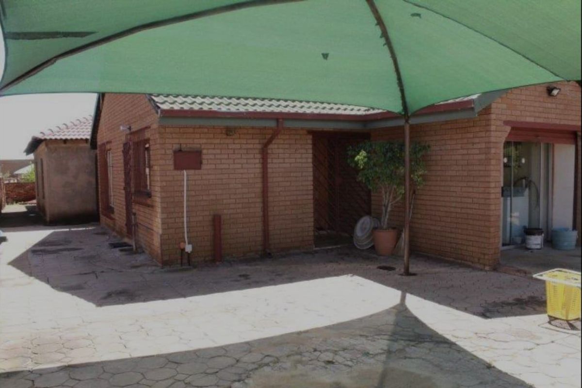 Rear exterior view of a face brick house featuring a paved patio area covered by a large green shade sail.
