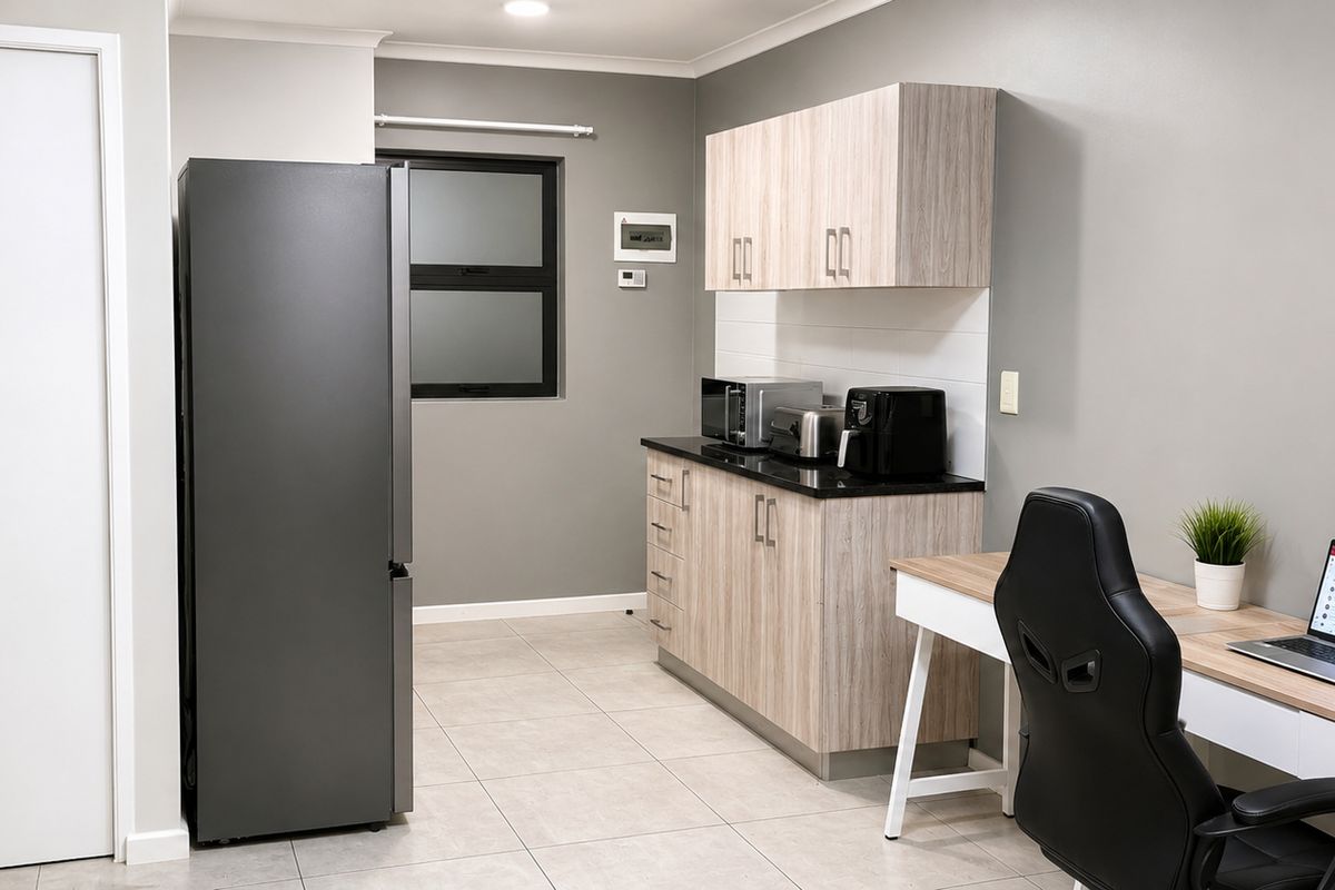 A modern kitchen area featuring light wood-grain cabinetry, dark countertops, tiled flooring, and a frosted window, integrated into a multi-functional living space.