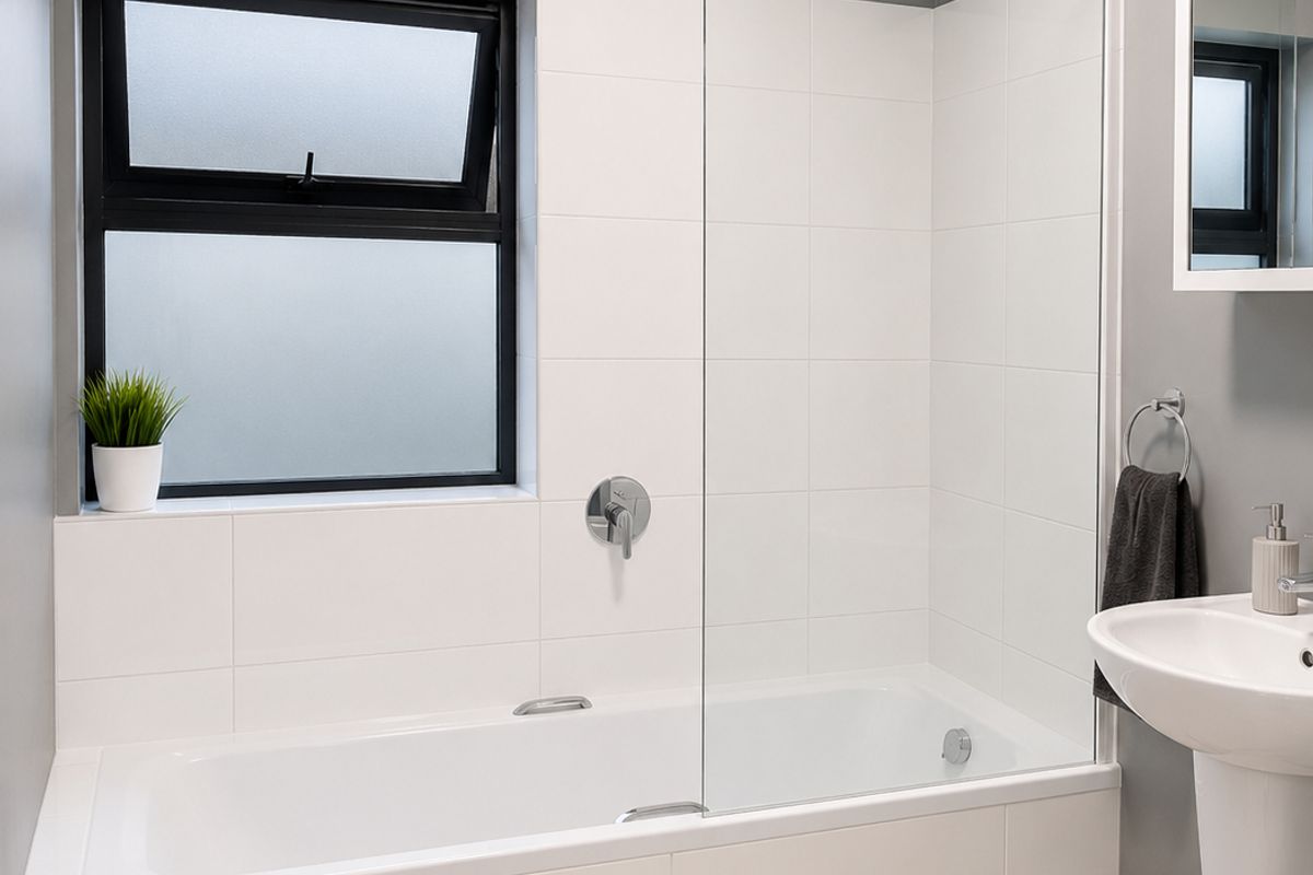 Modern bathroom featuring a white bathtub with a glass shower screen, pedestal sink, and neutral tiled finishes with a contemporary grey accent wall.