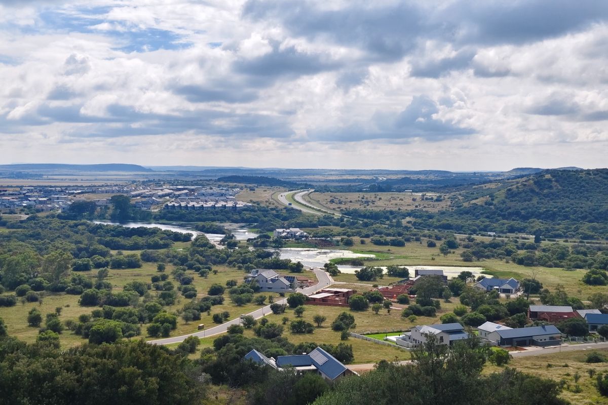 An elevated aerial view showcasing the surrounding landscape, local road infrastructure, and nearby residential developments in a scenic setting.