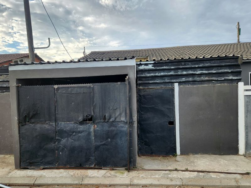 Street-facing garage structure featuring metal doors and corrugated roofing, showing significant signs of wear and weathering.