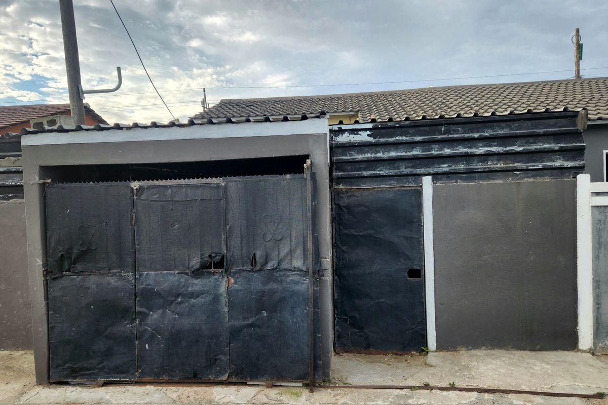 Street-facing garage structure featuring metal doors and corrugated roofing, showing significant signs of wear and weathering.
