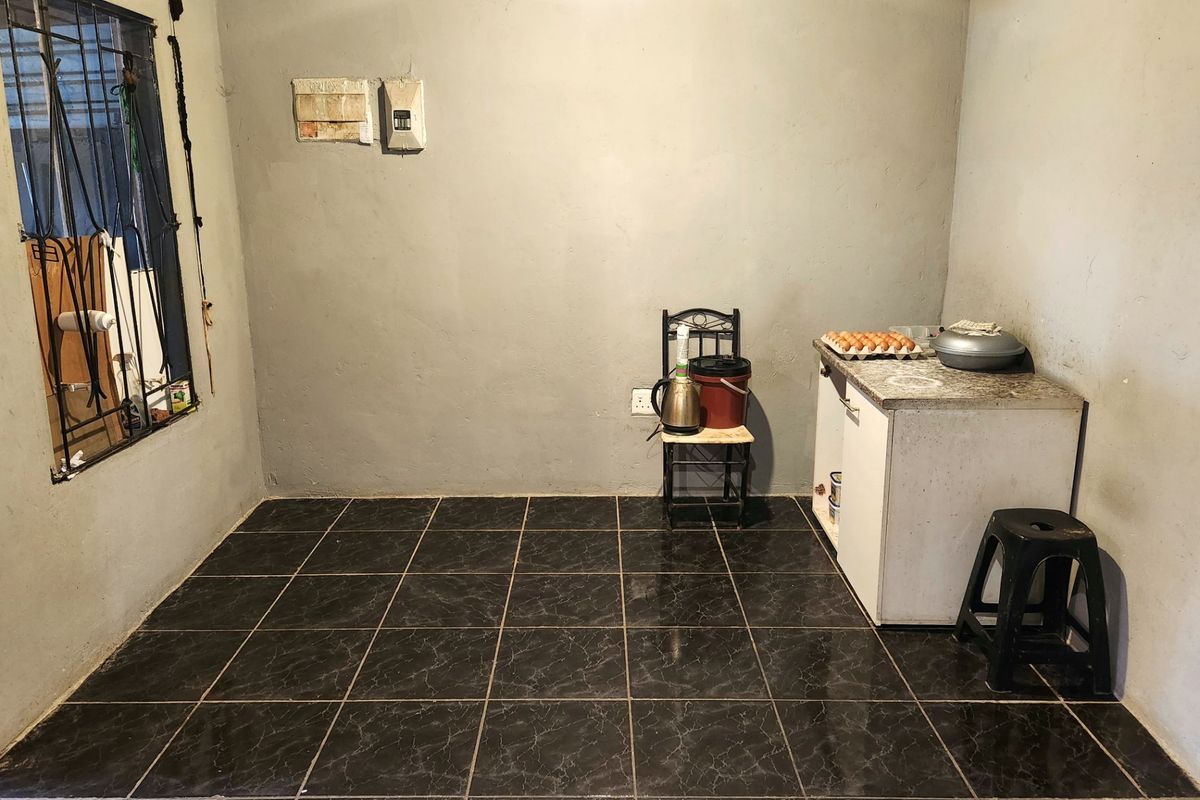 A basic kitchen area featuring dark tiled flooring, timber ceiling, and minimal base cabinetry with a stone countertop.