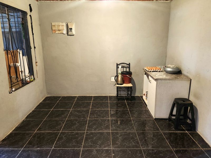 A basic kitchen area featuring dark tiled flooring, timber ceiling, and minimal base cabinetry with a stone countertop.
