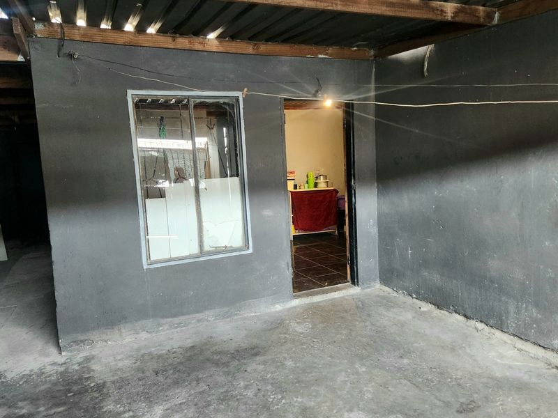 A covered outdoor patio area featuring concrete flooring, exposed timber rafters, and a metal-framed window, providing a functional transition space to the interior.