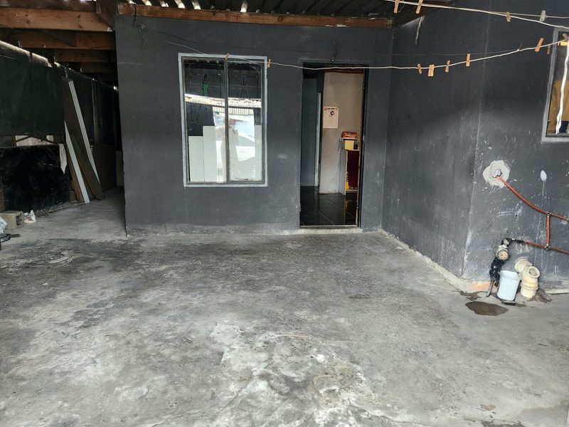 A covered outdoor patio area featuring exposed timber rafters, concrete flooring, and visible external plumbing connections.